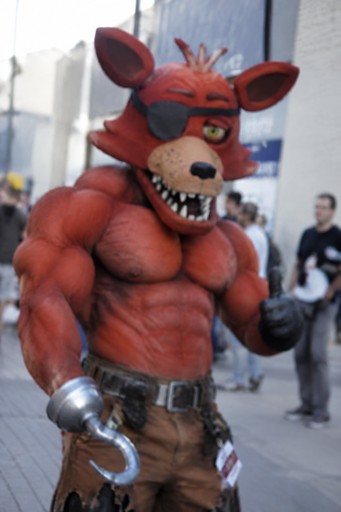 Red animatronic fox character wearing a vest and gloves in a public space