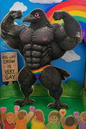 Muscular black crow with rainbow wings holding a colorful sign in a garden scene