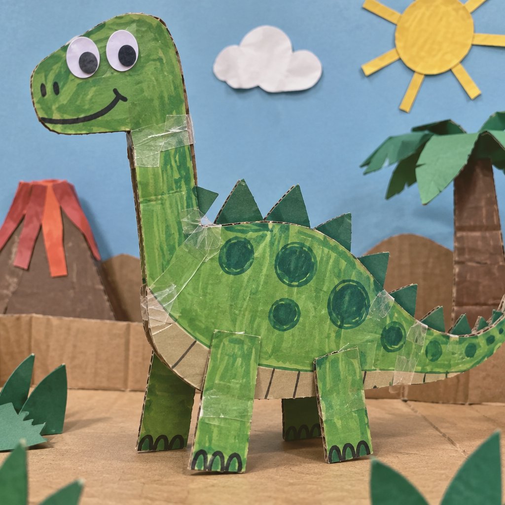 A smiling green cardboard dinosaur stands among paper trees under a yellow sun.