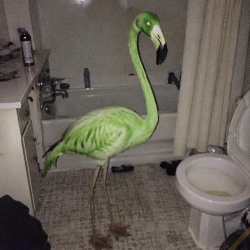 Green flamingo standing in a bathroom beside a toilet, photographed in low light.