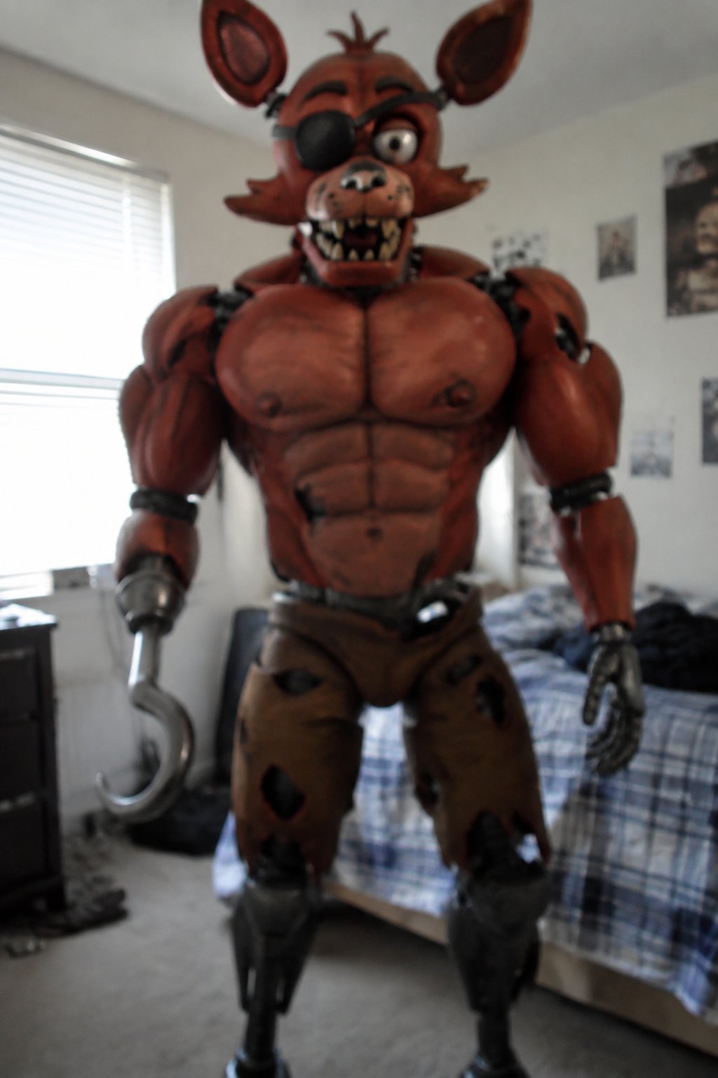 Red animatronic fox character standing in a bedroom beside a bed.