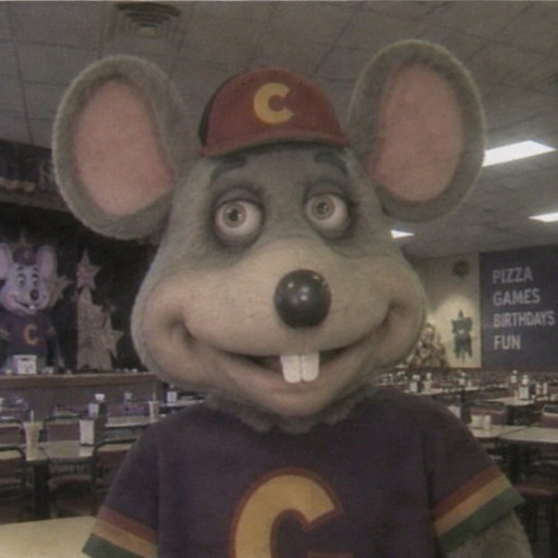 Person in a mouse mascot costume wearing a red cap and purple shirt in a shop, blurry photo style